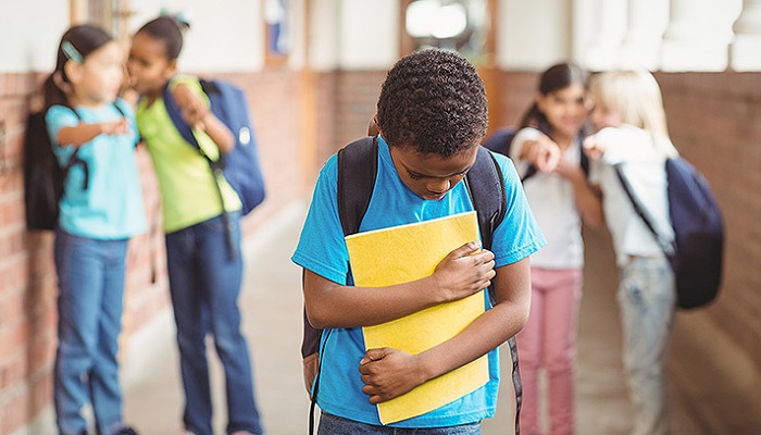 Sad pupil being bullied by classmates at corridor in school